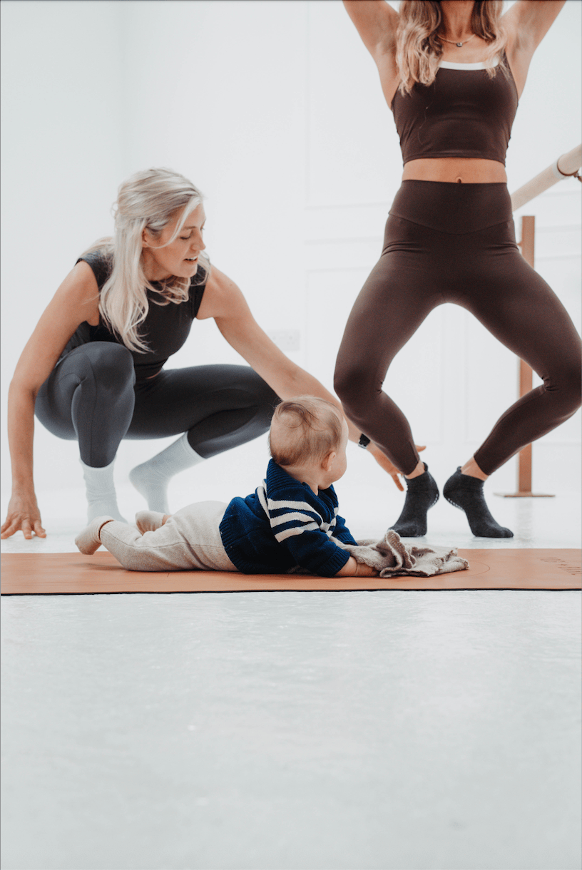 Barrecore instructor guiding postnatal fitness class with mother and baby, focusing on safe movement and bonding in studio setting.
