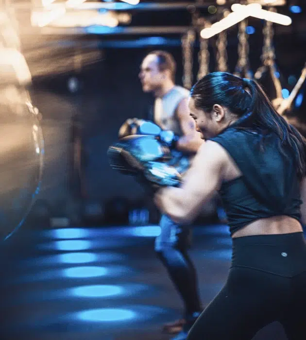 KOBOX client throwing punches during a high-intensity boxing and HIIT class, set in a nightclub-inspired studio with immersive lighting and energy.