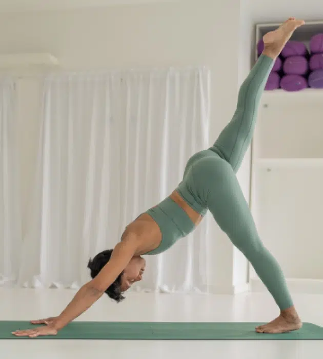 Triyoga student in a serene studio practicing Three-Legged Downward Dog, combining breath, balance, and mindful movement in a holistic yoga class setting.