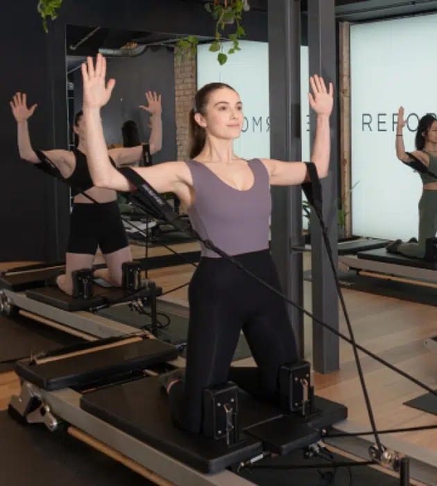Reformcore clients performing an upper body exercise on the Reformer, targeting posture, upper body strength, and core control in a contemporary Pilates studio.