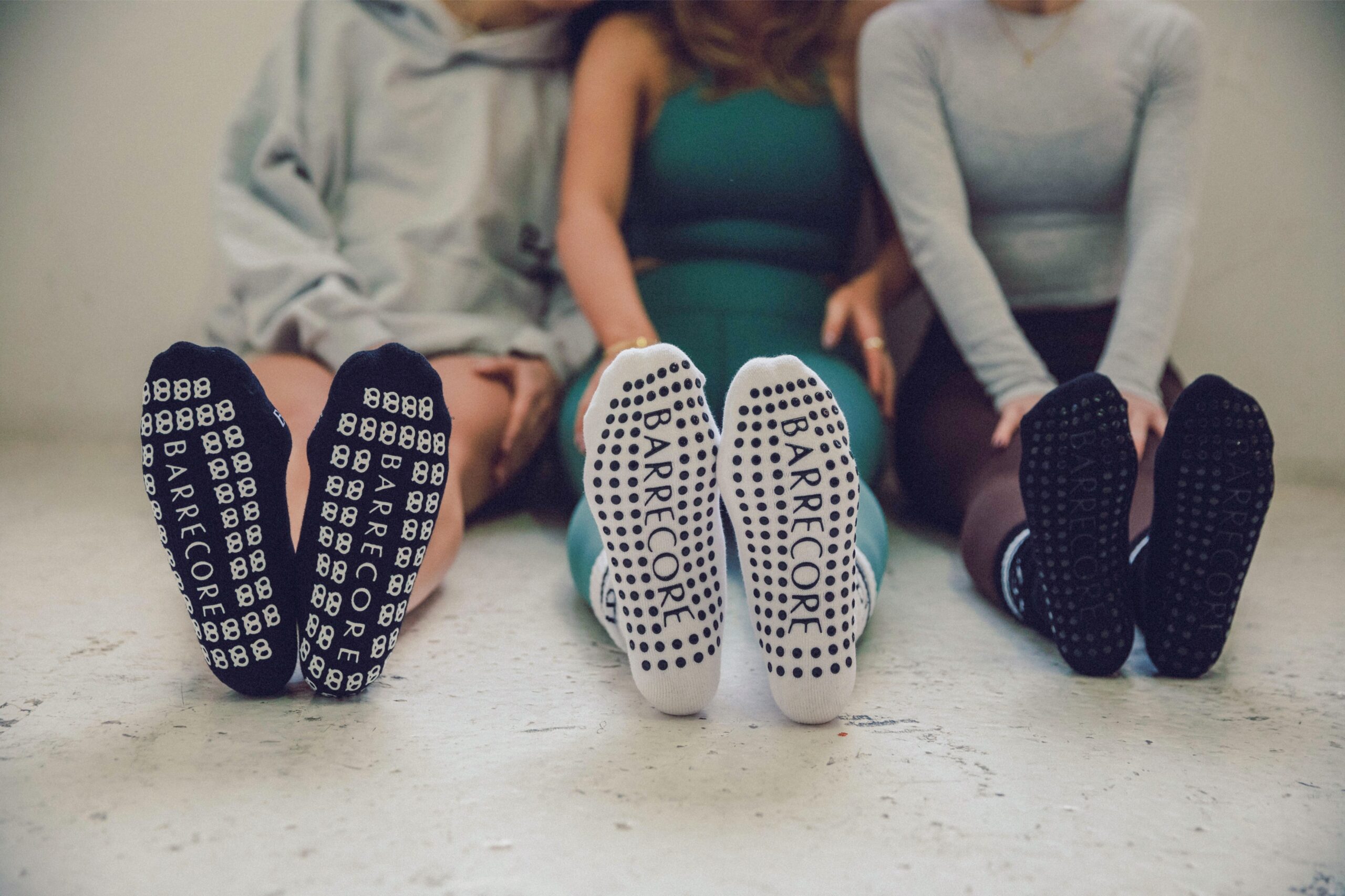 Close-up of three women wearing branded Barrecore grip socks, seated on studio floor after class.